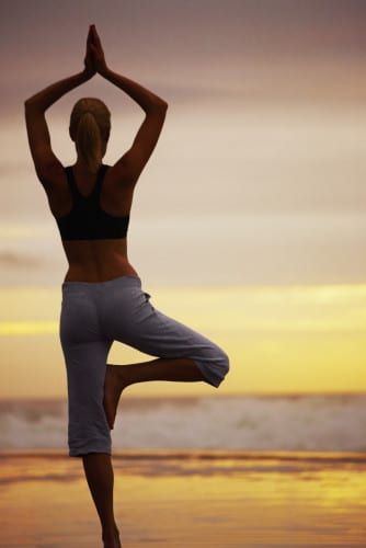 Rear view of a female practicing yoga in a tree pose by the sea during sunset
